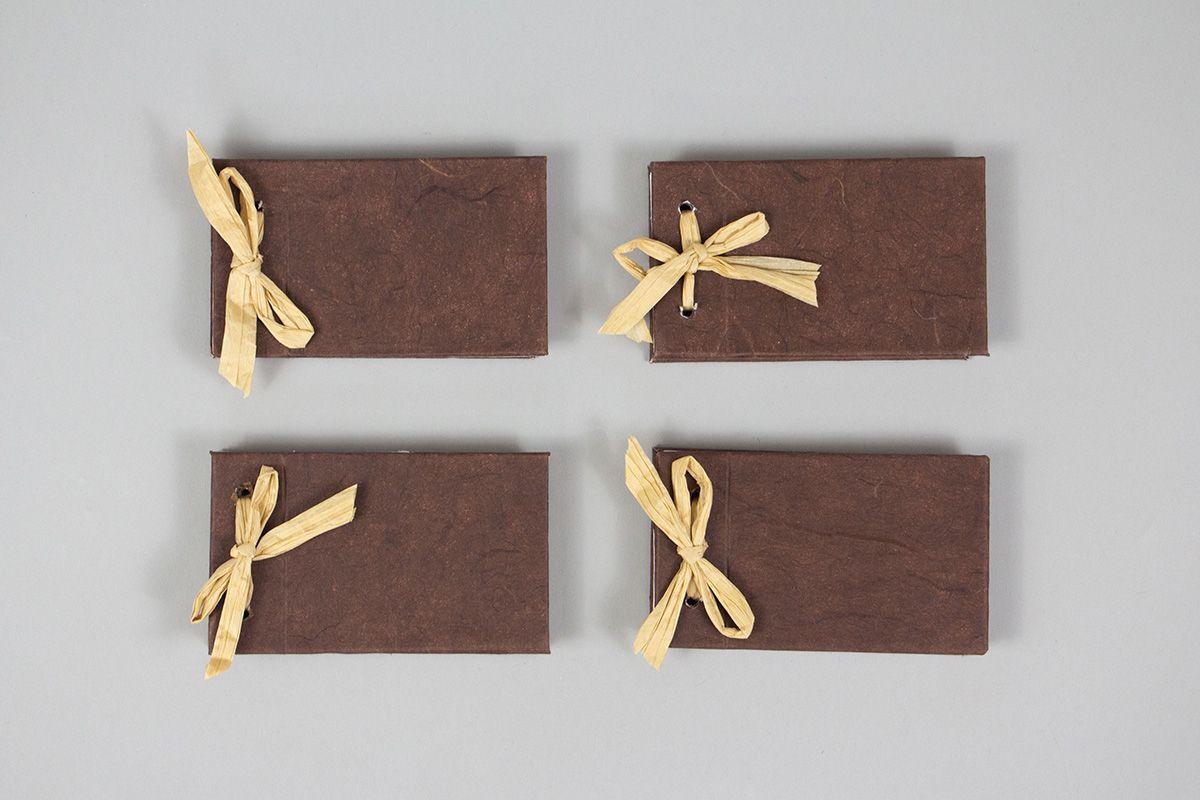 Four miniature brown books with a raffia ribbon binding